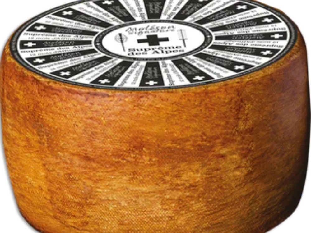 A barrel-shaped Suprême des Alpes cheese featuring its natural rind and a label on top.