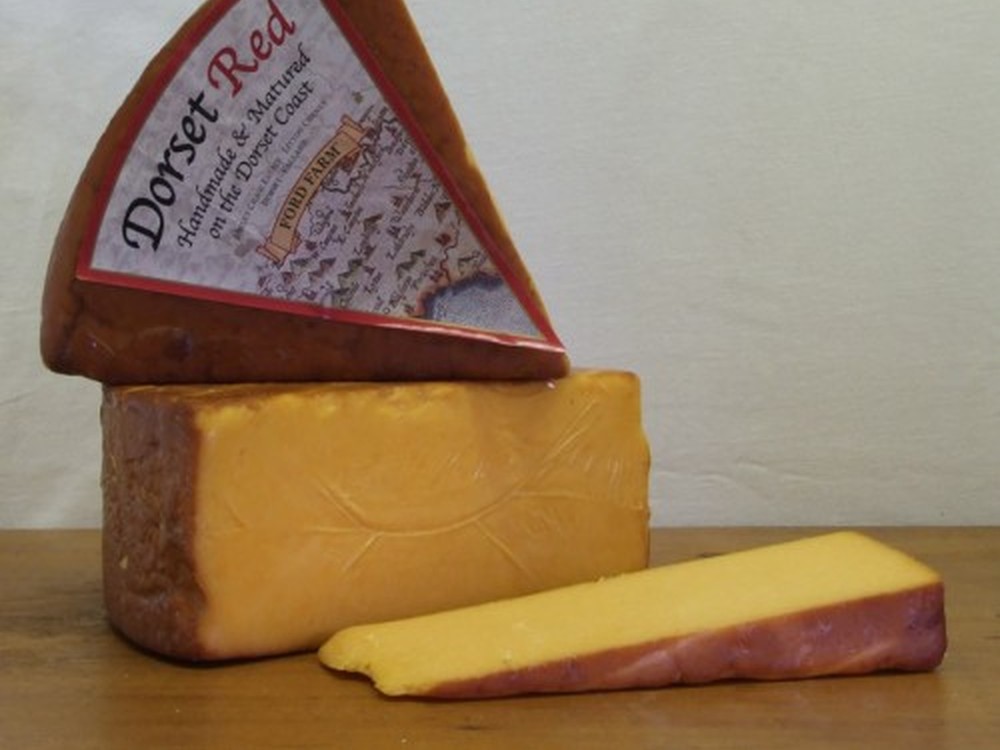 Slices of Dorset Red cheese are stacked on a wooden surface, with one slice displaying its label, set against a white background