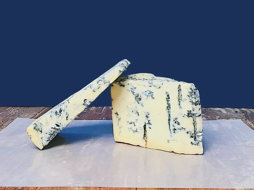 Slices of Gorgonzola Piccante DOP cheese, with its blue veins on a creamy interior, are arranged on butter paper on a wooden surface