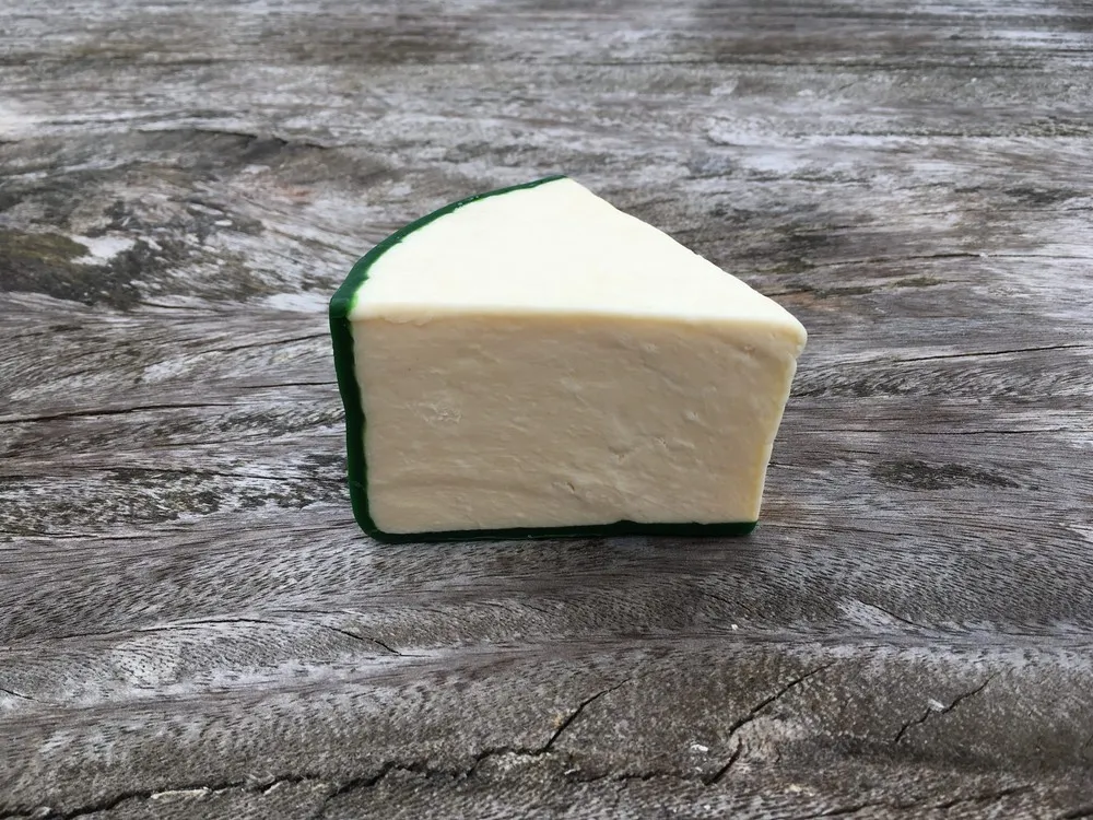 A slice of Mature Yorkshire Wensleydale cheese, with a pale yellow interior and green wax rind, rests on a wooden surface