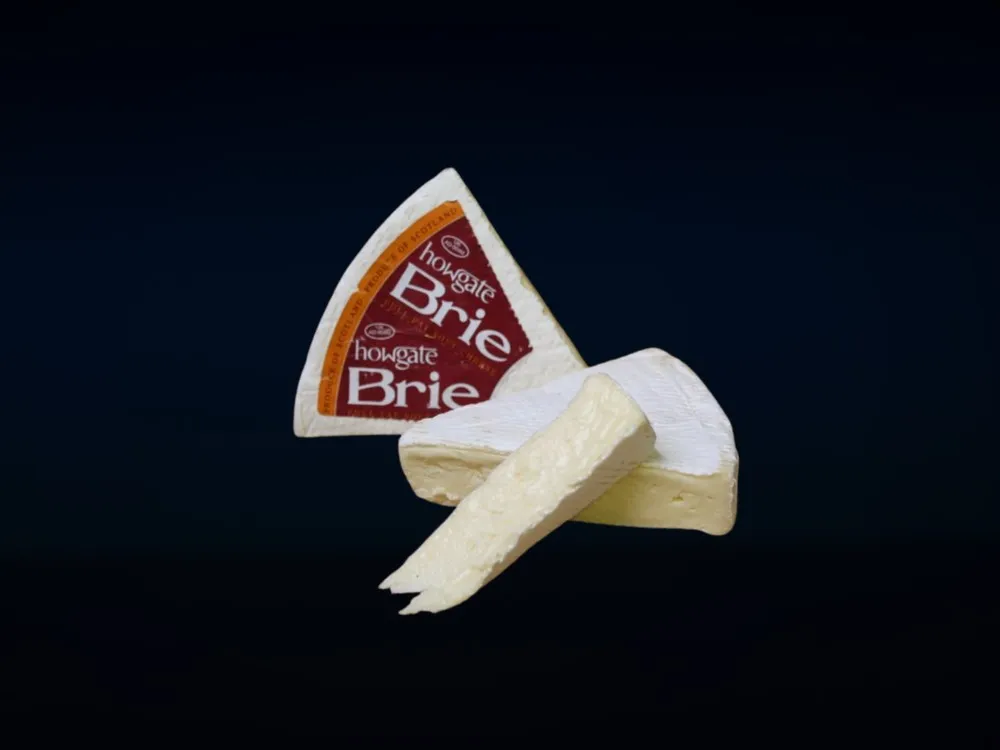 Triangular pieces of Howgate Brie Cheese, displaying a bloomy rind and creamy interior, with a label, set against a black background