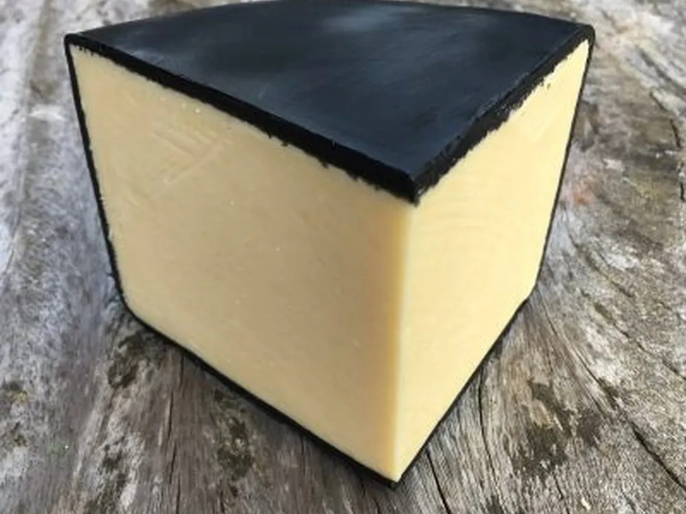 A wedge of Just Jane Cheddar cheese, encased in black wax, rests on a wooden surface