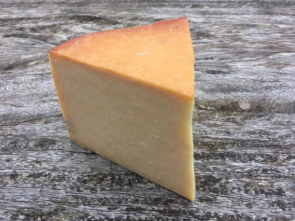 A triangular piece of Smoked Lancashire cheese rests on a wooden surface