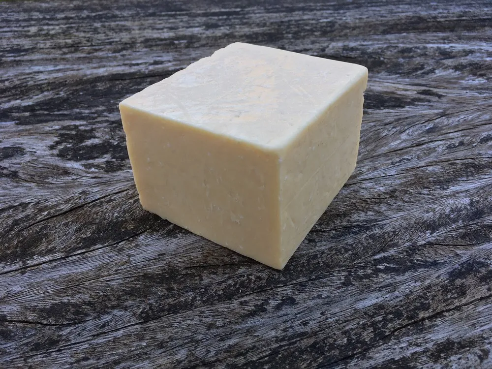 A block of Coastal Cheddar cheese placed on a rough wooden surface