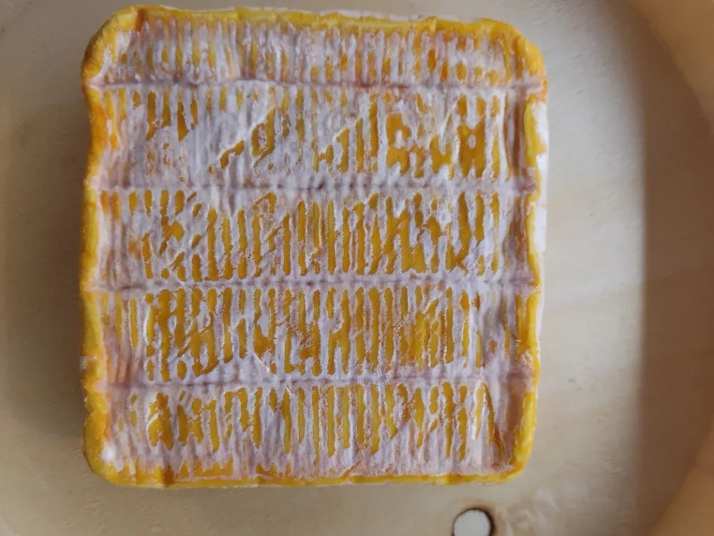 A square-shaped Minger cheese with its orange rind, placed on beige paper