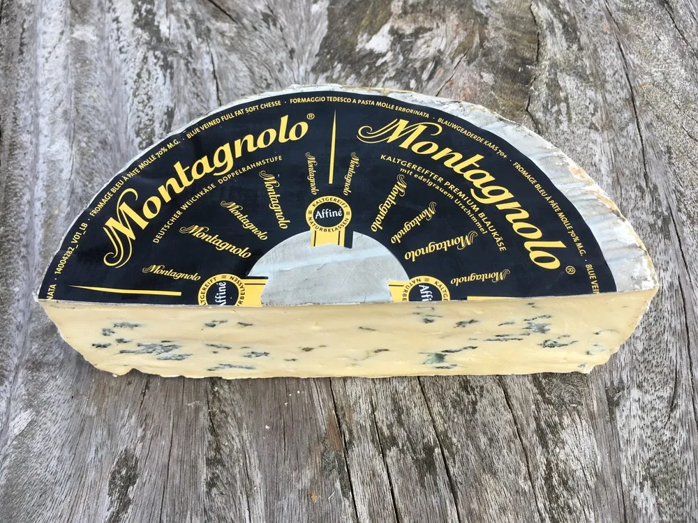 A halved wheel of Montagnolo cheese, labeled on top, reveals its creamy blue-veined interior, resting on a rustic wooden surface