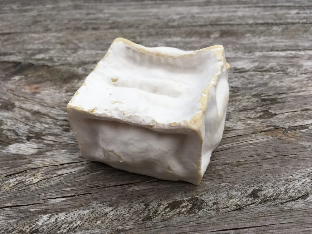 A square-shaped Pavé d'Affinois with its ivory bloomy rind rests on a wooden surface