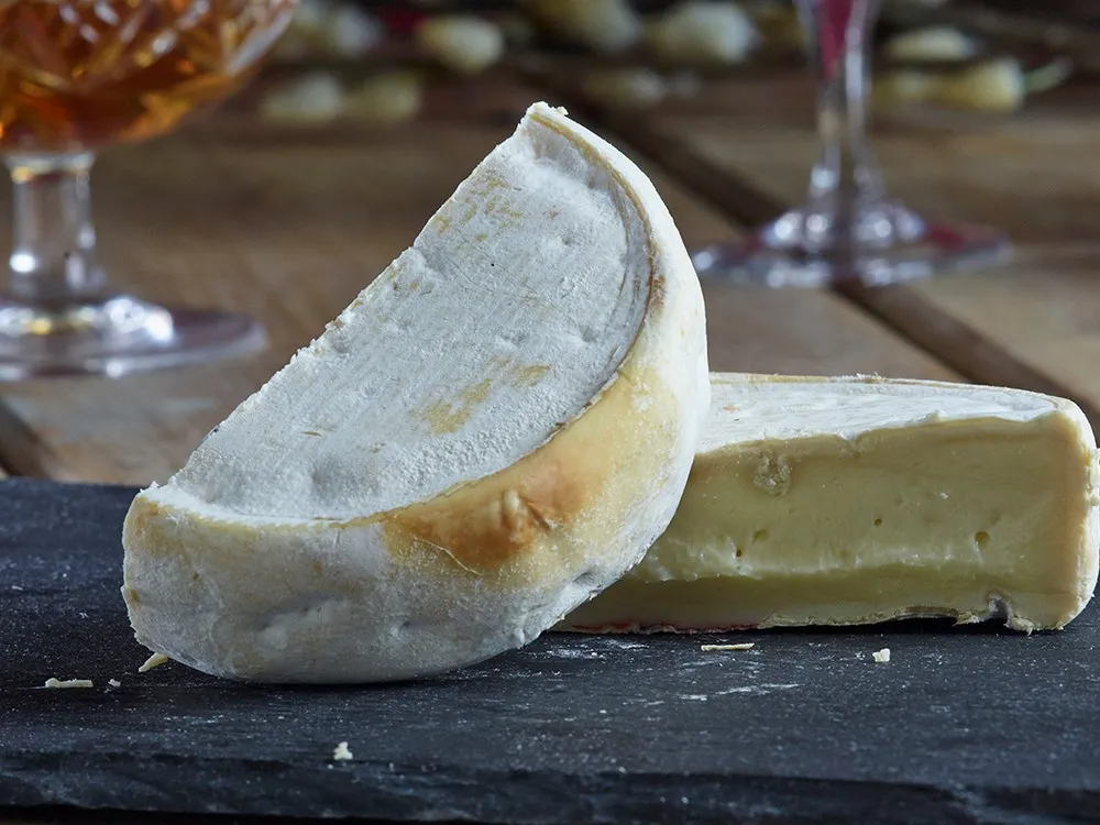 A wheel of Reblochon cheese, cut in half to reveal its smooth interior and mold-covered rind, rests on a black marble