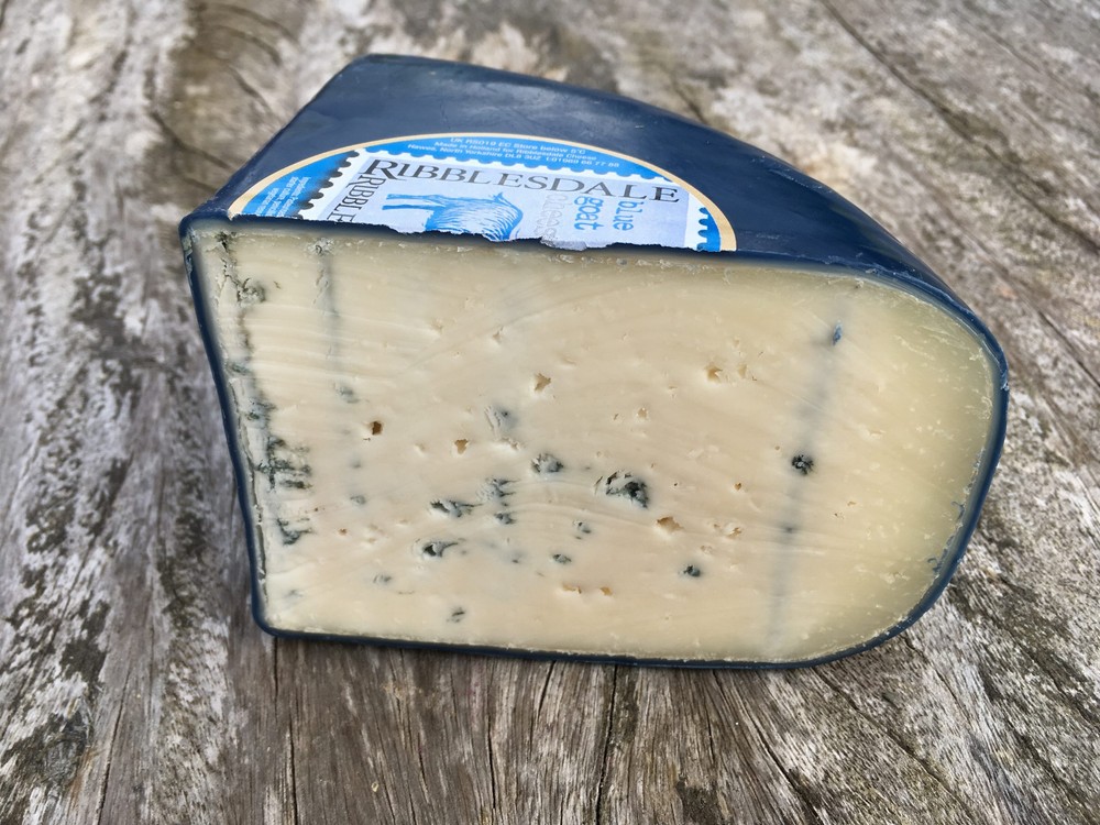 A slice of Ribblesdale Blue Goat cheese, coated in blue wax, resting on a wooden surface