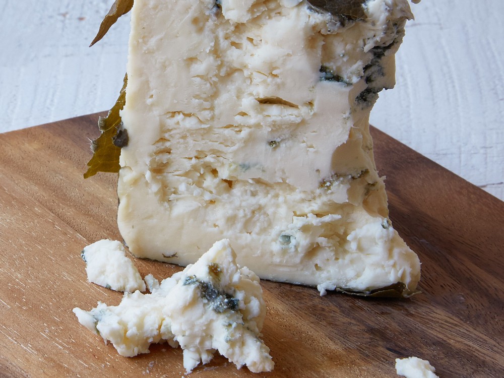 A piece of Rogue River Blue cheese, revealing its smooth texture and intricate blue veins, with a portion of Syrah grape leaves resting on a wooden surface