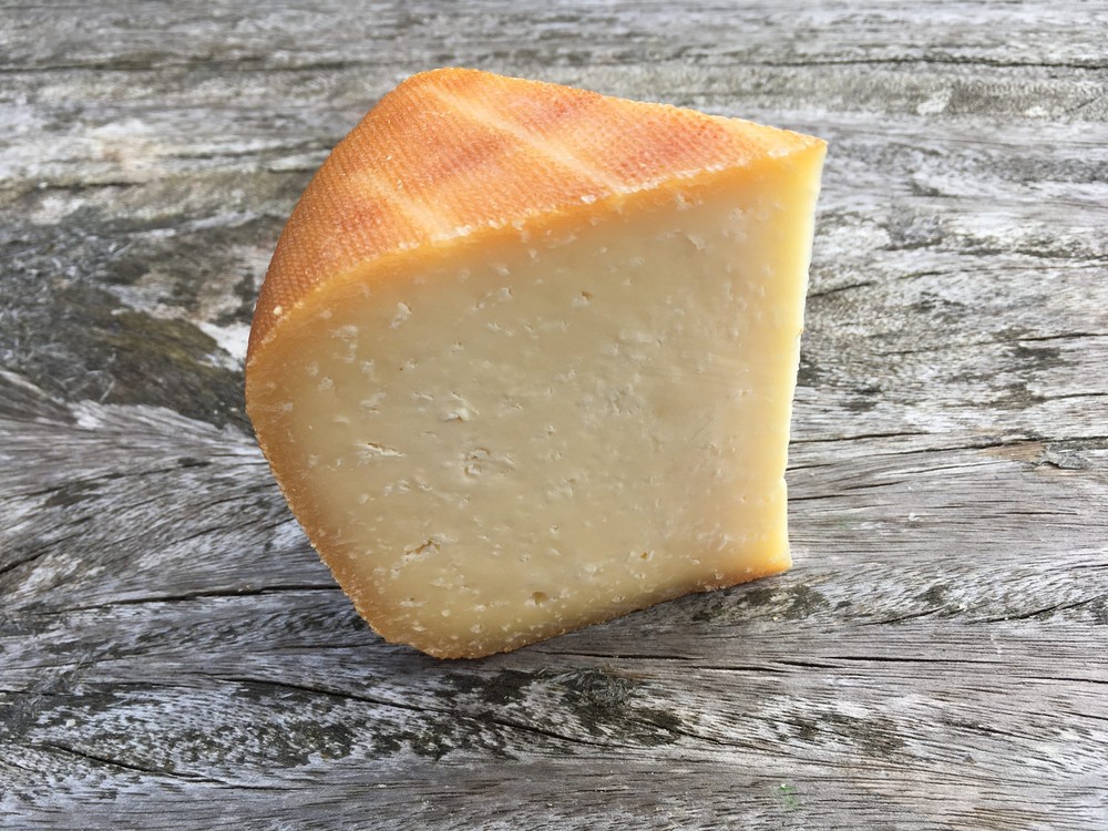 A slice of Lyburn Lightly Oak Smoked cheese with a golden-brown rind, displaying smooth interior on a wooden board