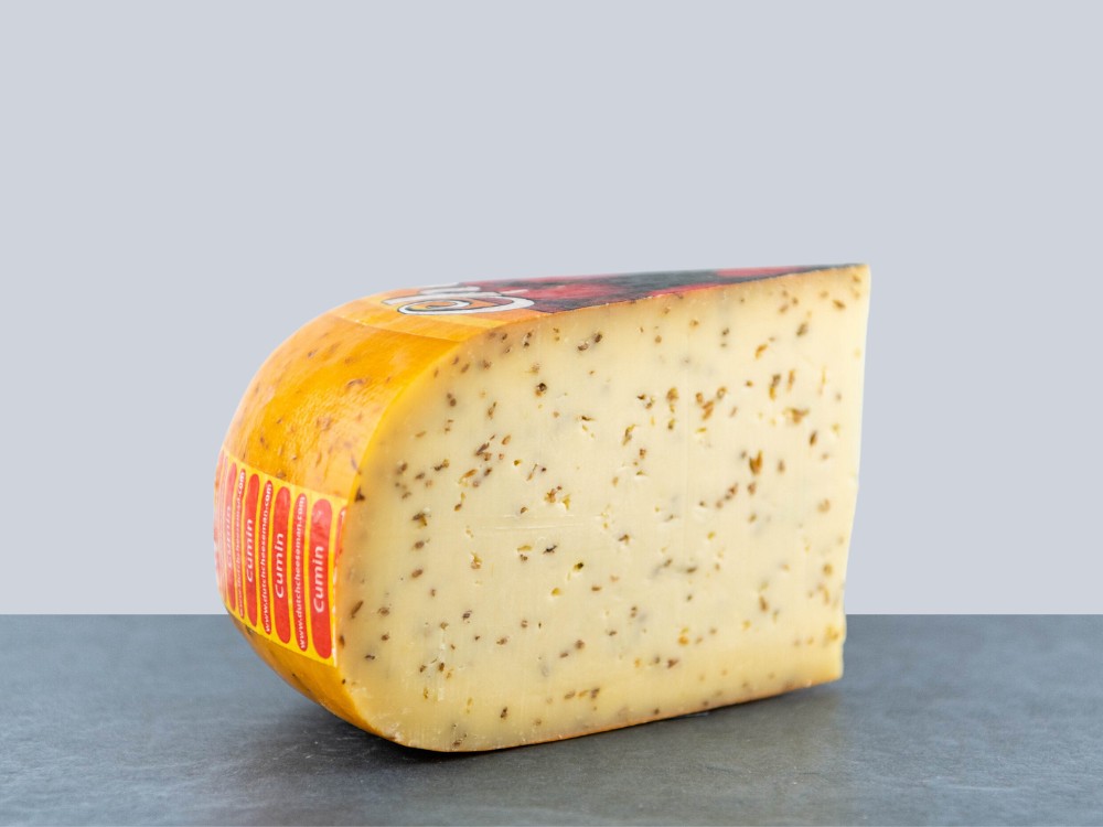 A slice of Cumin Gouda, its smooth texture and creamy consistency accented by cumin seeds, set against a grey background