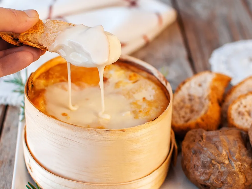 A Vacherin cheese on bread reveals its creamy, gooey, and soft paste. It's often baked in its wooden box until fully melted and runny