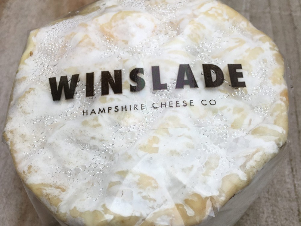 A disc of Winslade cheese, wrapped in a white sheet, reveals its cream-colored interior and bloomy rind