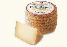 A cylindrical P'tit Basque cheese with a slice cut to showcase the distinctive basket-weave pattern on its rind