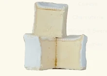 Stacked, partially cut Brillat-Savarin cheeses revealing their soft interior and delicate, white bloomy rind, set against a white background