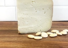 A slice of Ossau-Iraty cheese with an ivory-colored interior rests on a wooden surface, accompanied by blanched almonds