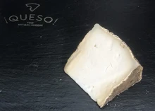 A slice of Garrotxa cheese, showcasing its ivory interior, rests on a black marble surface