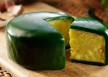 A partially cut truckle of Green Thunder cheese, encased in emerald-colored wax, rests on a wooden board