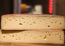 A Fontina Val D'Aosta cheese wheel, cut in half and stacked, showing its pale cream interior with distinctive "eyes"