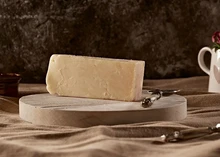 A wedge of Isle of Mull cheese sits on a round wooden cutting board, accompanied by a cheese knife