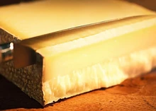 A cheese knife slices through Kaltbach Le Gruyère, a Swiss AOP cheese with a pale yellow interior and a dark, rustic rind