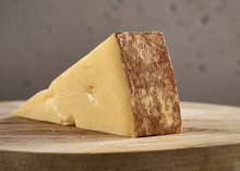 A slice of Lincolnshire Poacher cheese, displaying its yellow interior and brownish rind, resting on a wooden surface