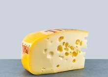 A slice of a Maasdam cheese with a dark rind, revealing smooth yellow interior with eyes (holes).