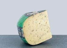 A wheel of Nettle cheese with a slice cut out displayed on a flat surface