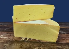 Wedges of Ogleshield cheese, revealing their creamy color, are stacked on a wooden surface