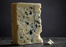 A slice of Roquefort cheese, revealing its smooth, creamy interior with blue veins, placed on a black surface