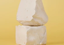 Pieces of Shamembert, a vegan cheese, showing creamy interior and natural rind, are arranged against a yellow background