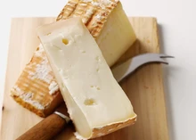 Wedges of Taleggio cheese with a creamy yellow texture and orange rind sits next to a cheese knife, showcasing its soft interior and wrinkled rind.