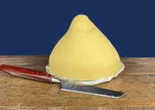 A pear-shaped, pale yellow Tetilla cheese, with a sharp knife nearby, rests on a wooden surface