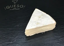 A triangular piece of Wigmore cheese showcasing creamy and soft paste beneath the rind placed on a black marble