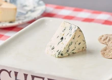 A slice of Yorkshire Blue cheese revealing blue veins on a pale yellow interior placed with crackers on a white plate