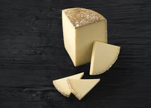 Slices of Cantal cheese revealing its pale yellow interiror and natural rind placed on a black wooden surface