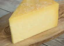 A triangular piece of Finlay's Cheddar cheese, highlighting its rich yellow interior, rests on a wooden surface