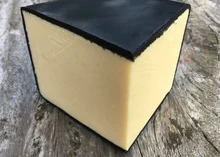 A wedge of Just Jane Cheddar cheese, encased in black wax, rests on a wooden surface