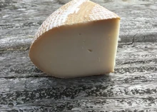 A slice of Rachel cheese with pale yellow interior kept on a wooden surface