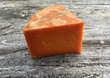 A slice of Red Leicester, displaying its vibrant orange hue from annatto, sits on a wooden surface