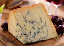 A slice of Colston Bassett Stilton, showcasing its creamy interior marbled with blue veins, is paired with fresh cherries on a wooden surface