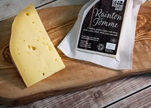 A slice of Rainton Tomme cheese, accompanied by its packaging, rests on a wooden board