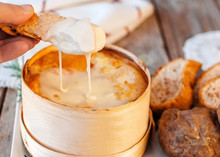 A Vacherin cheese on bread reveals its creamy, gooey, and soft paste. It's often baked in its wooden box until fully melted and runny