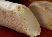 Logs of Ragstone cheese, showcasing their fudgy texture, are set against a maroon background