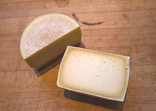 Romano cheese, cut in half to reveal its grainy texture and hard, brittle rind, resting on a wooden surface