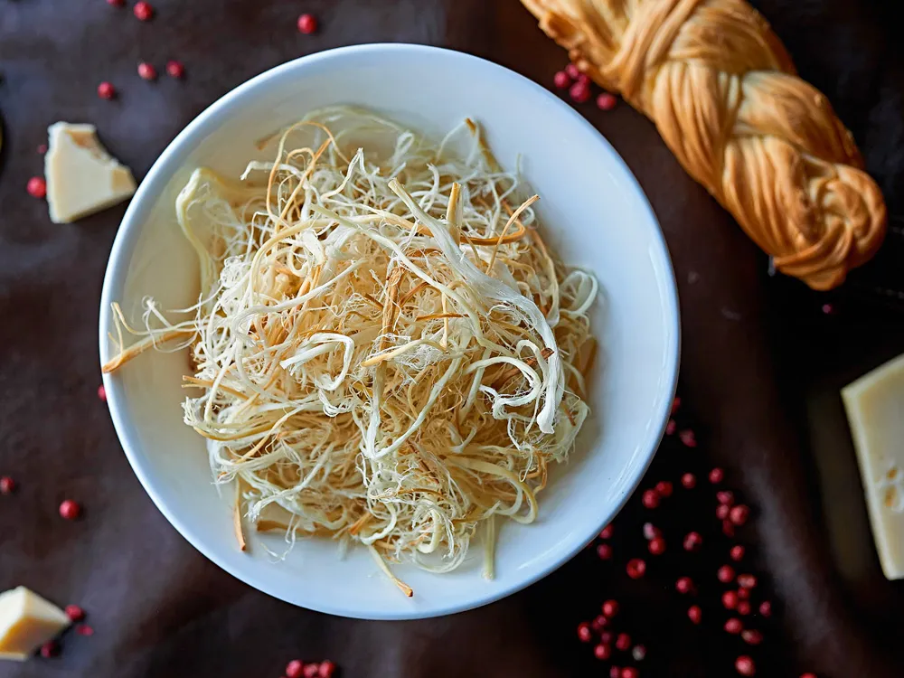 Armenian String Cheese (Chechil) is served on a white plate, accompanied by cheese slices and strings of Chechil