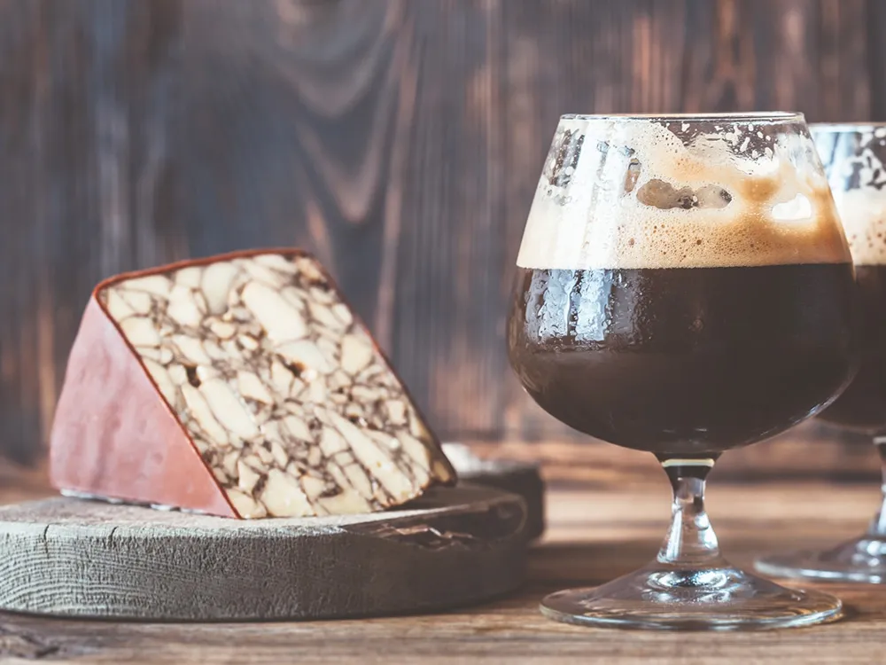 A wedge of Original Irish Porter cheese rests on a round wooden surface, accompanied by a glass of porter wine, all set atop a wooden table