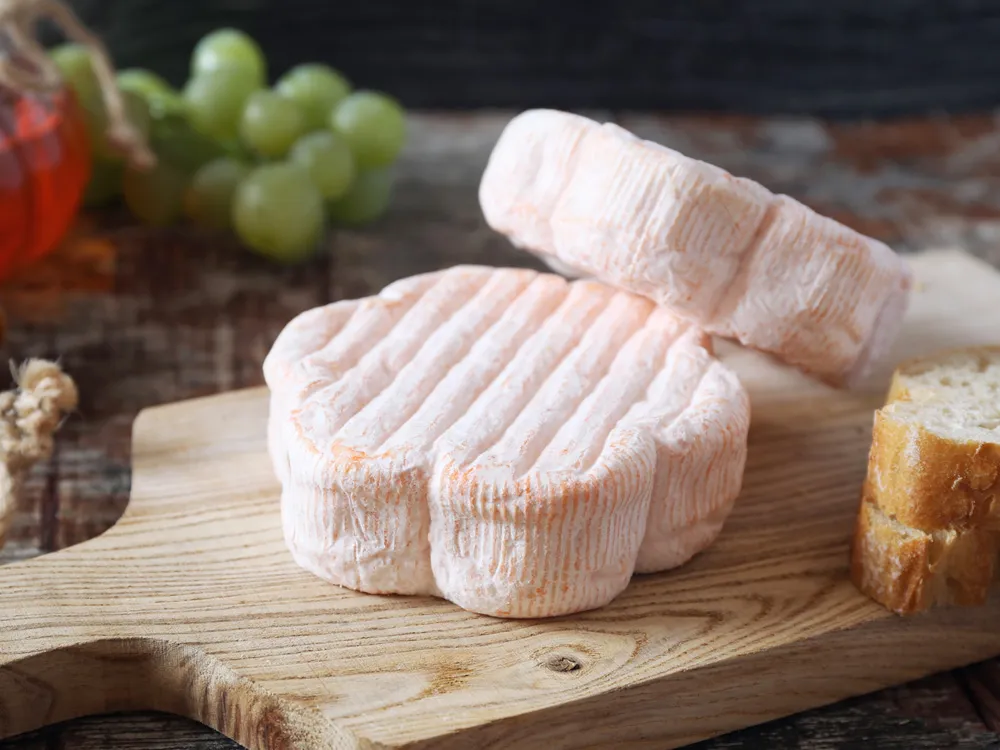 Floral-shaped Saint Albray cheeses are stacked on a cutting board, accompanied by slices of bread