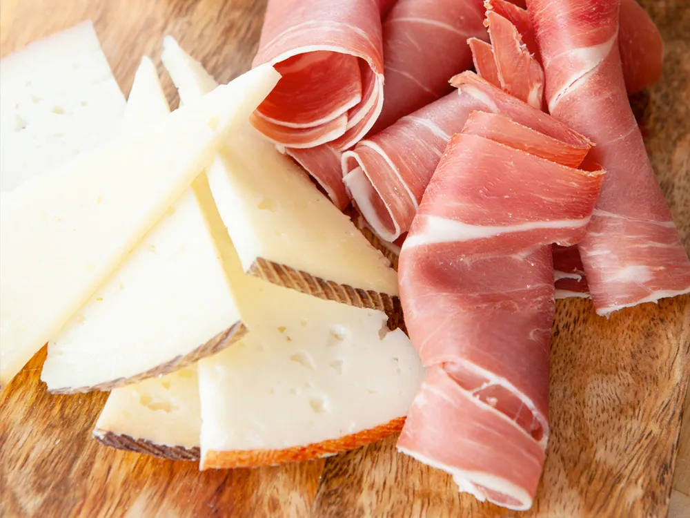 Thin slices of Queso Ibérico and ham elegantly arranged on a wooden board